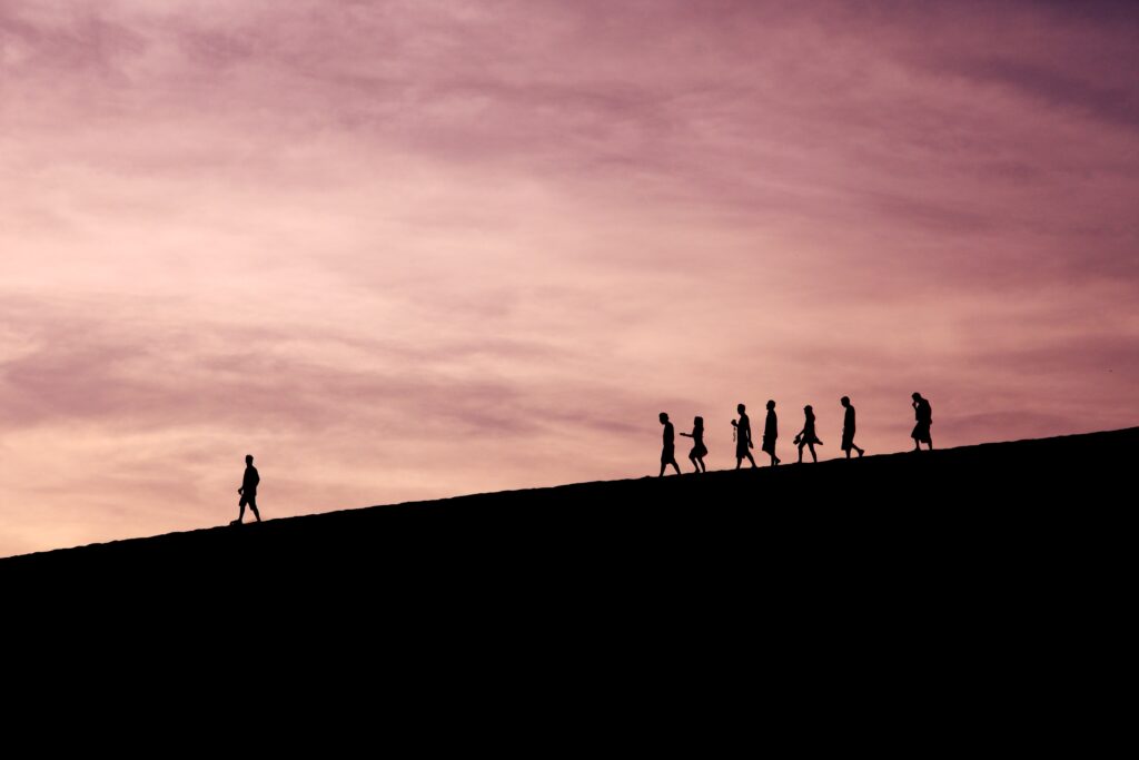 Silhouetten van een groep mensen die bij zonsondergang een heuvel afgaan