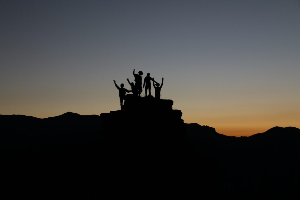 Silhouetten van een groep mensen die boven op een berg staat